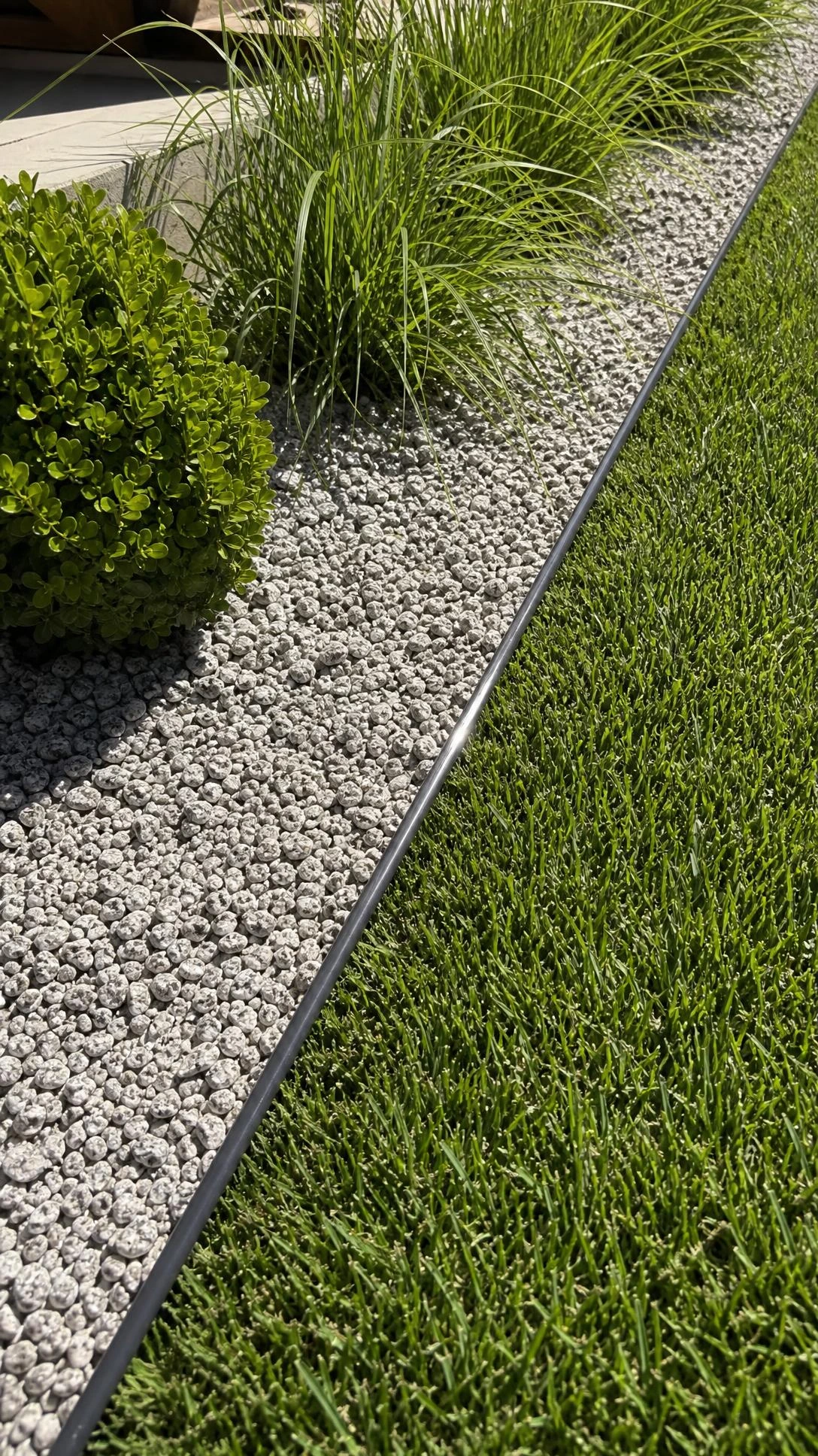 Thin charcoal powder-coated steel edging creating a razor-sharp border between lawn and garden bed, the minimal landscaping detail that looks professionally installed