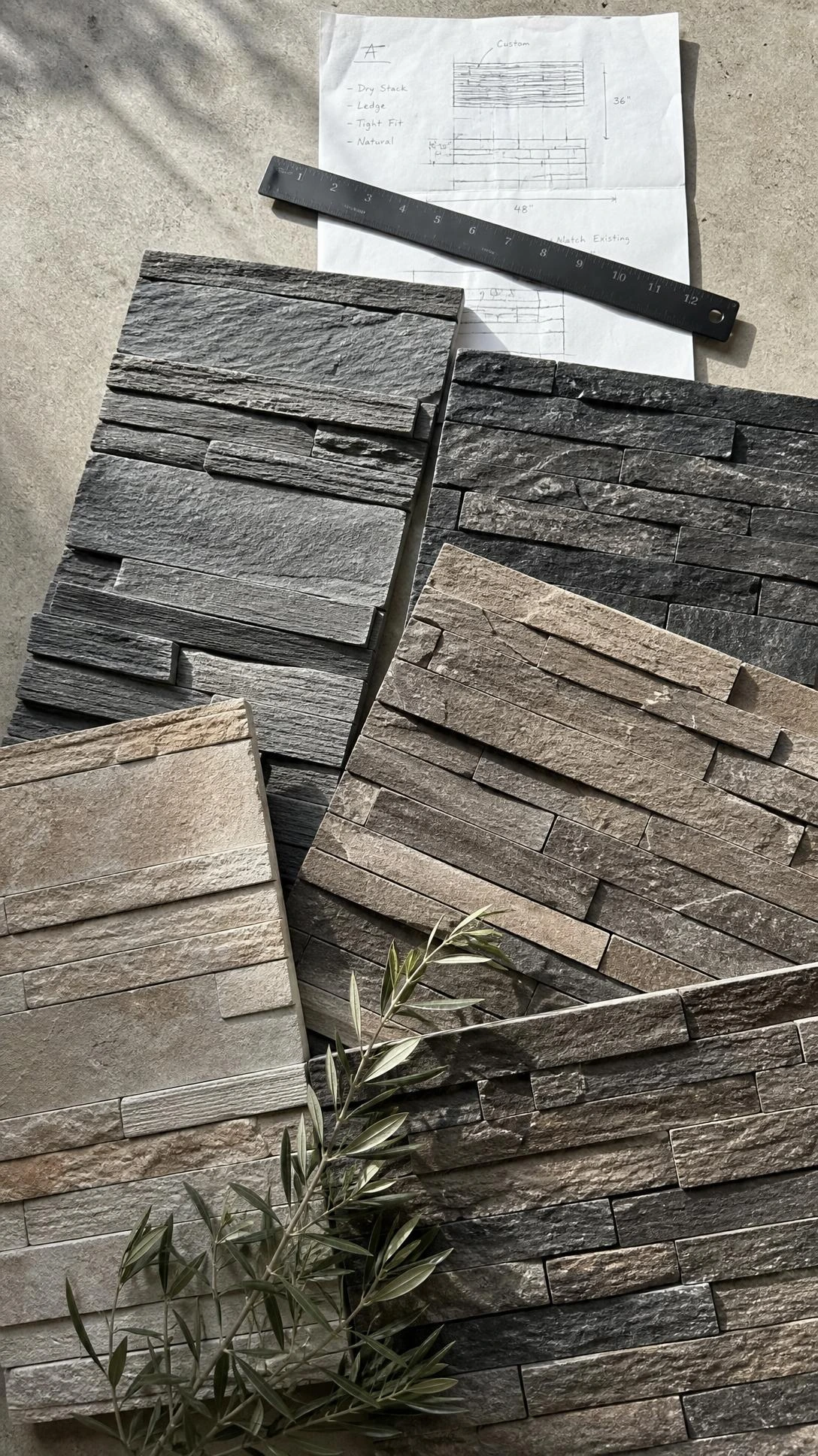 Stone look wall panel samples in slate gray, charcoal, taupe, and earthy beige arranged flat on concrete, showing realistic vein patterns and 3D texture depth for a TV feature wall