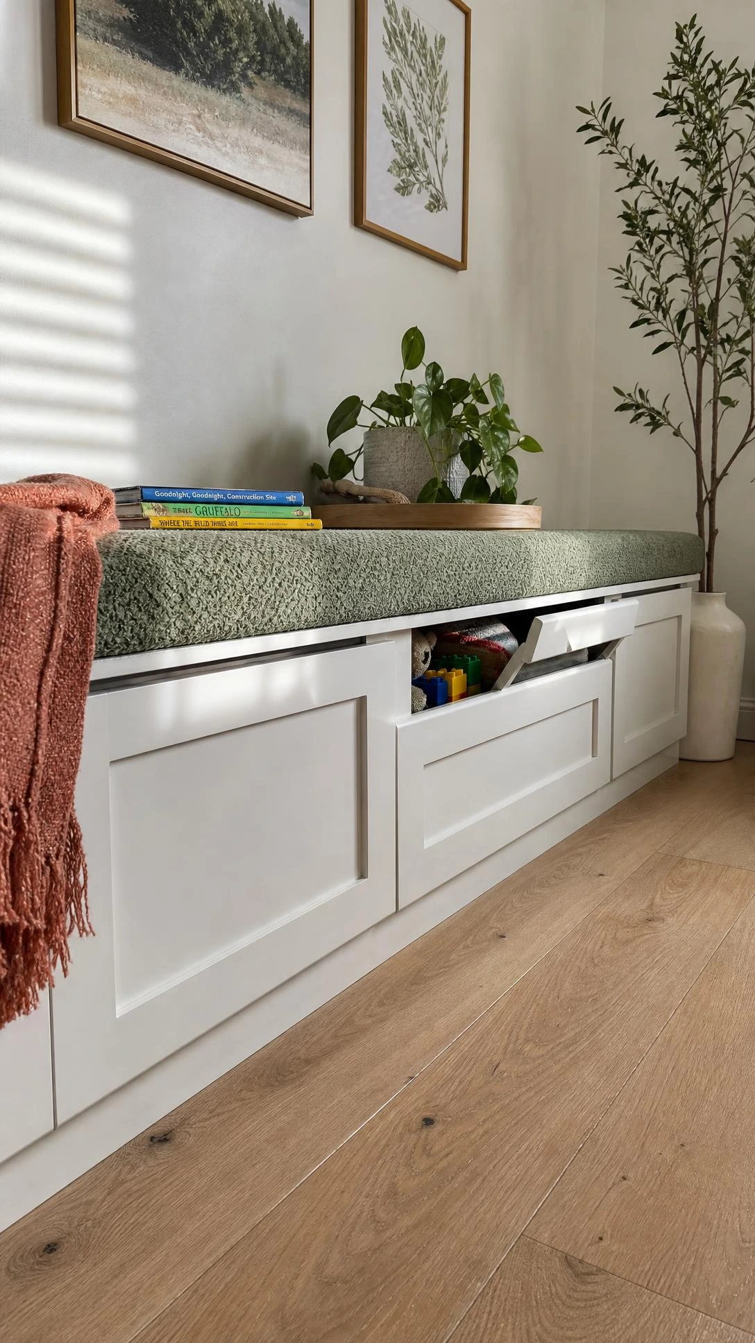 Sage green boucle storage bench with white lift-top compartments running the full length of a living room wall, keeping toy clutter completely out of sight