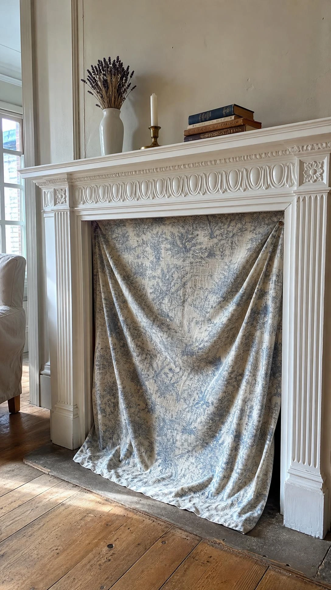 Victorian fireplace opening draped with flowing cotton fabric as a summer cover, framed by white-painted carved surround with egg-and-dart molding and fluted pilasters