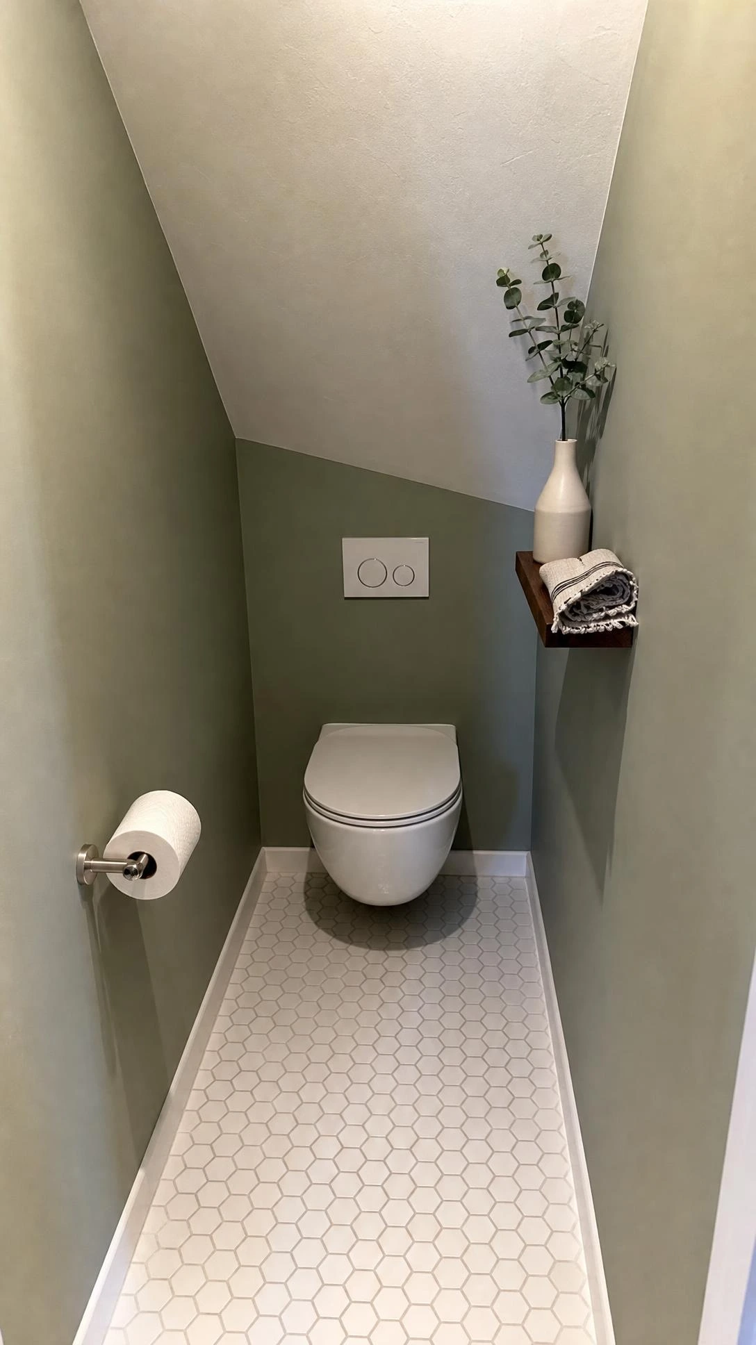 Wall-hung toilet positioned against the narrowest wall of a triangular under-stair bathroom, showing how toilet placement unlocks the entire compact floor plan