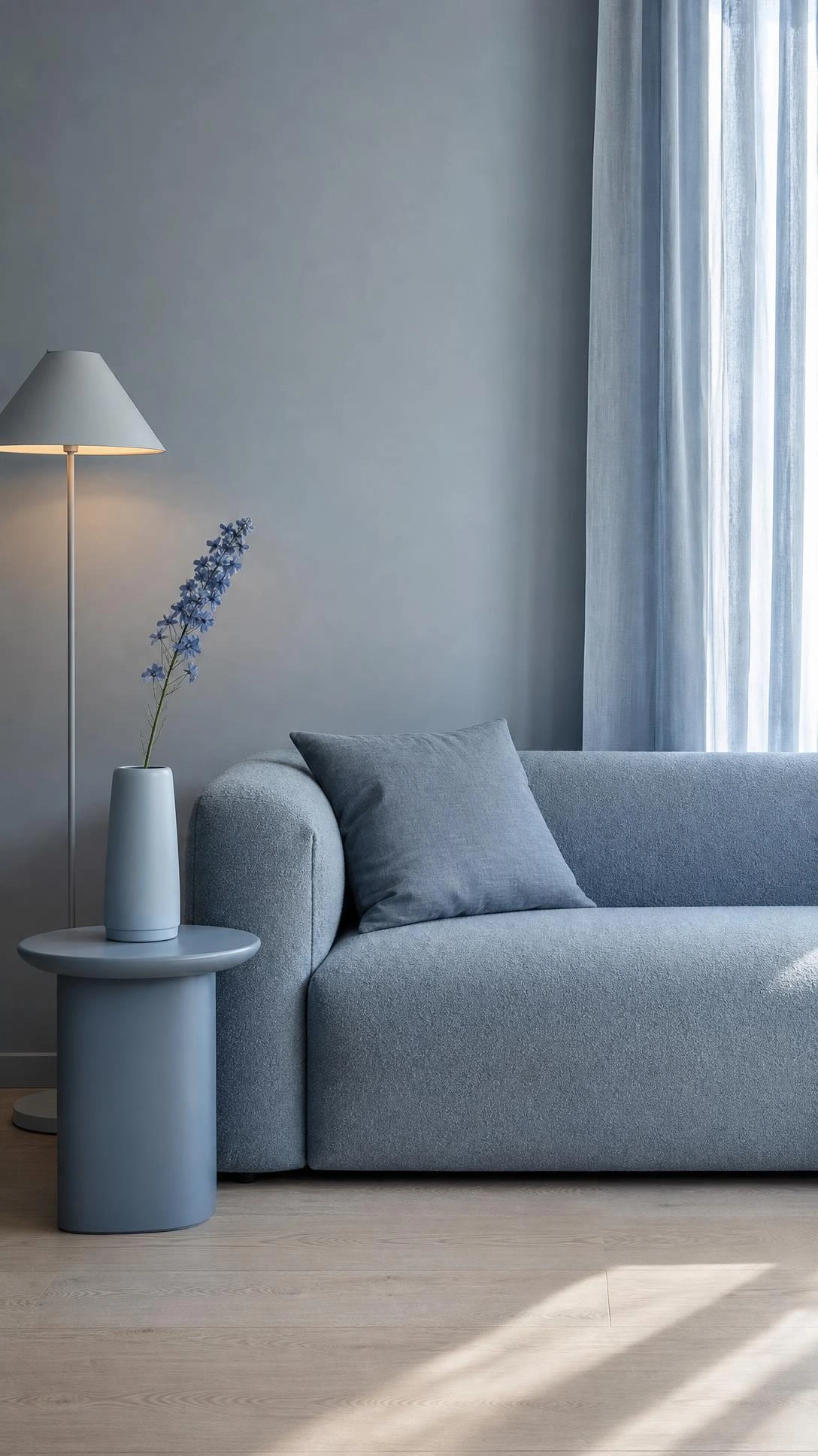 Minimalist living room corner styled in a single dusty blue tonal color scheme, with a sleek floor lamp and sheer curtains creating a calm, cohesive atmosphere