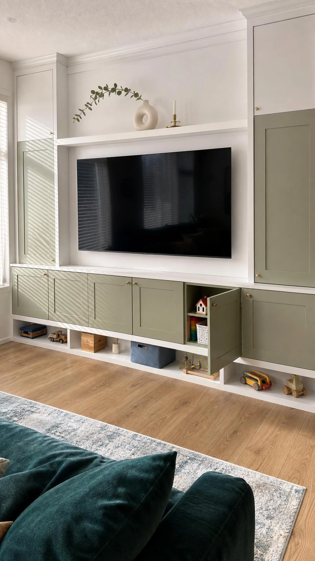 Built-in white MDF TV unit with hidden toy storage compartments below the flat-screen, keeping a stylish living room floor completely clear