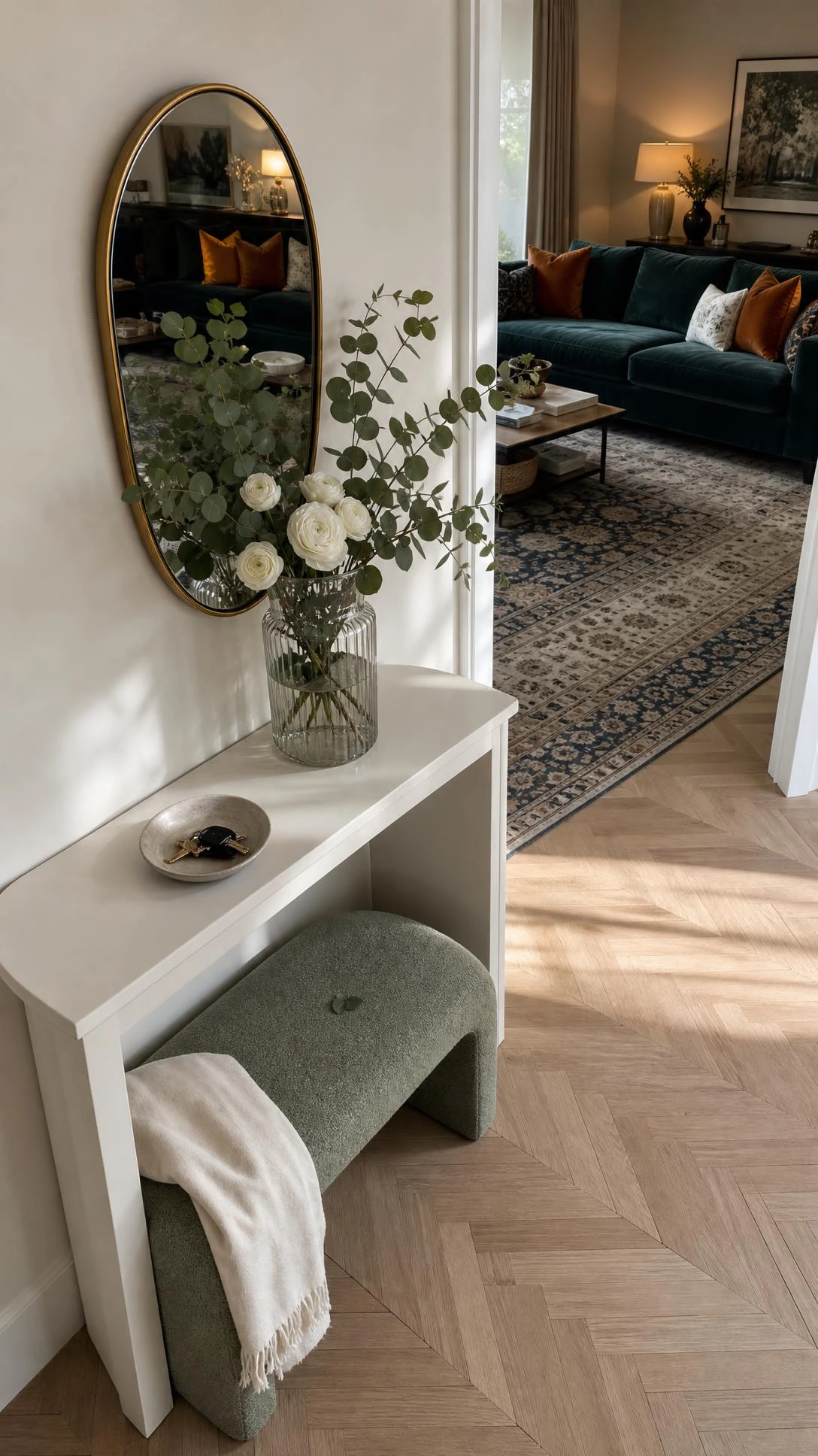 Slim oak console table with eucalyptus and white ranunculus arrangement marking the entryway transition into a chic living room