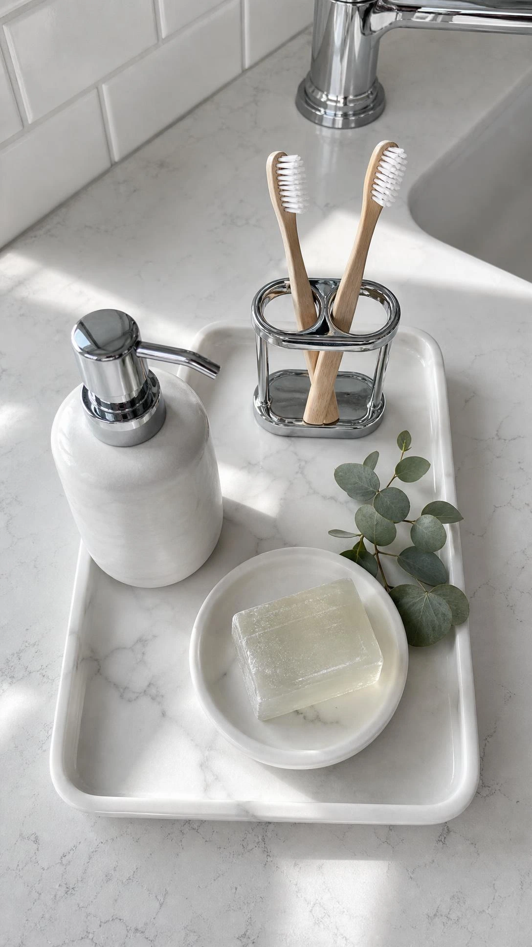 Overhead flat lay of white ceramic soap dispenser with chrome pump, toothbrush holder, and soap dish arranged on a marble-effect tray for a clean bathroom look