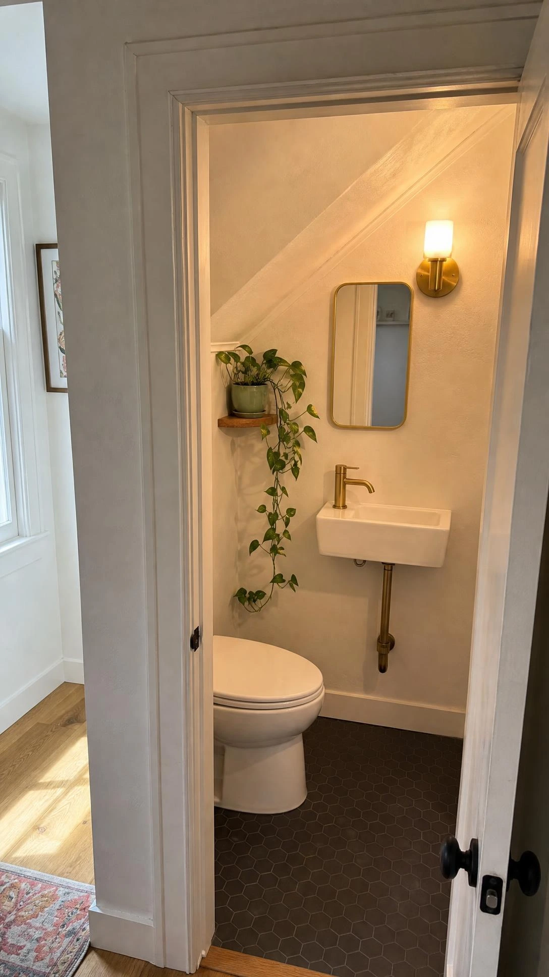 Compact under-stairs bathroom with angled ceiling following staircase slope, showing full functional layout through open doorway in a real home