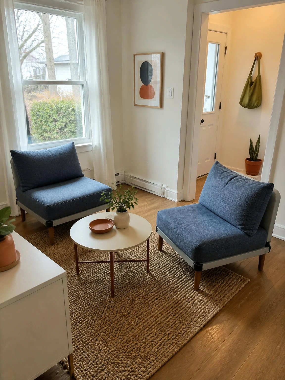 Two dusty blue armless chairs create flexible seating in a small living room while keeping the window and central walkway open