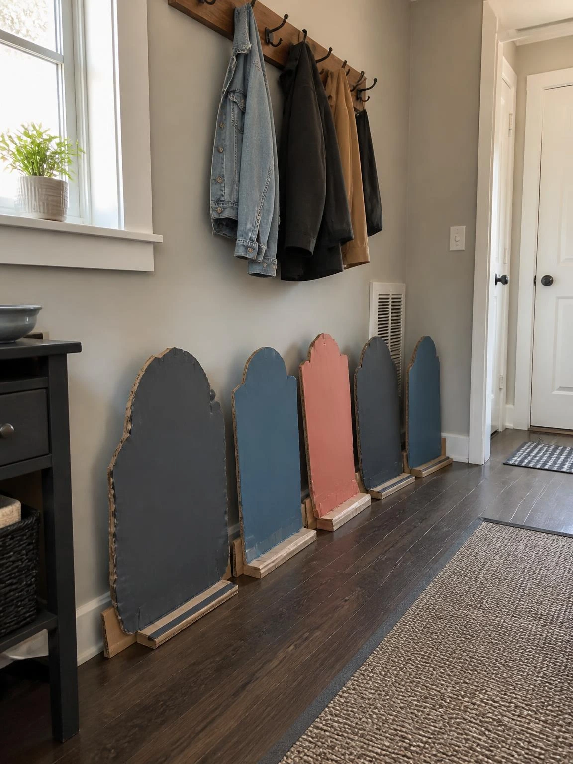 Hand-painted cardboard tombstones in soft coral, muted blue, and charcoal line a small hallway for cheap DIY Halloween decorations indoor.