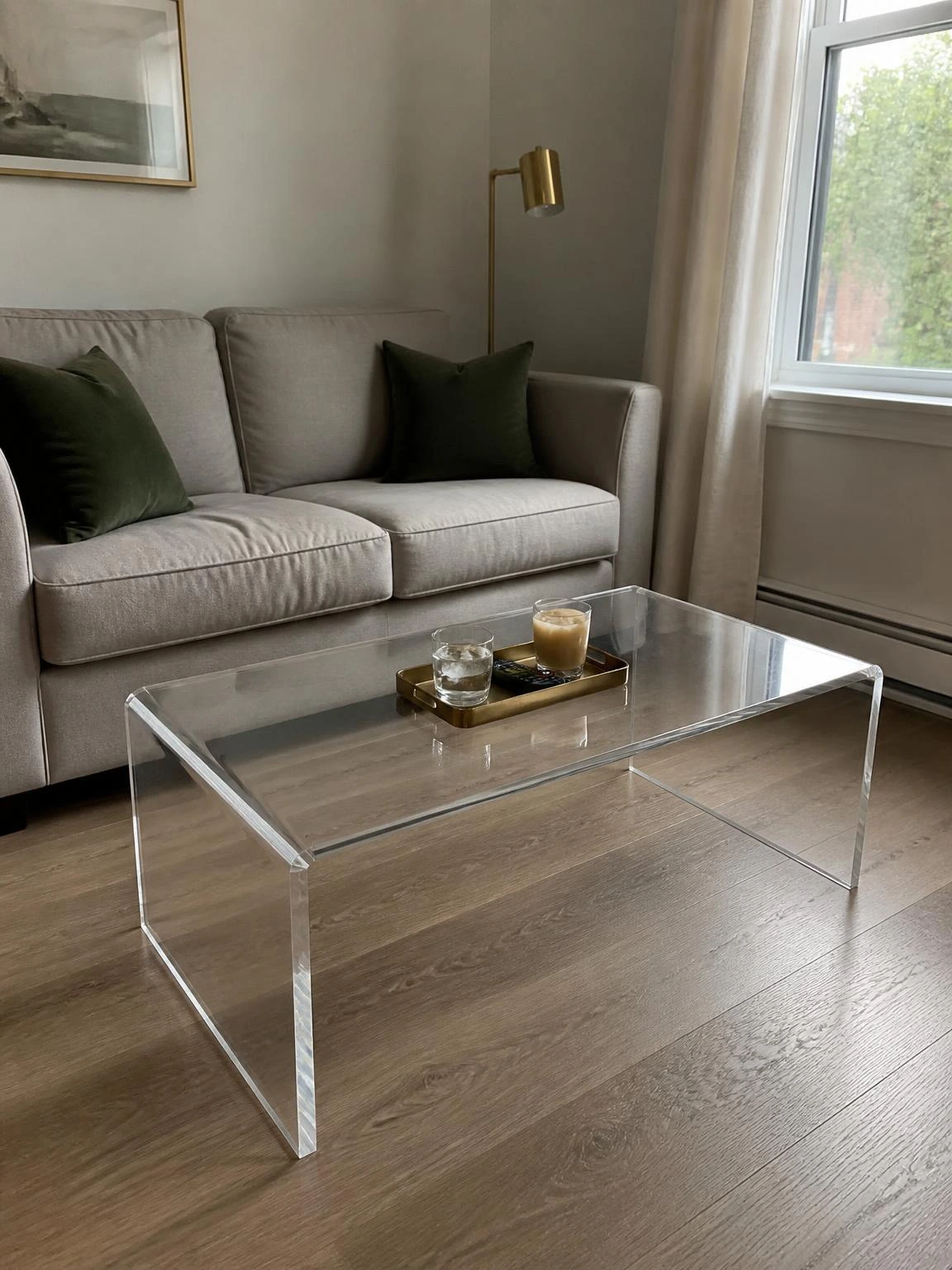 Clear acrylic coffee table in a tight living room preserves floor sightlines while providing useful surface space beside a gray sofa