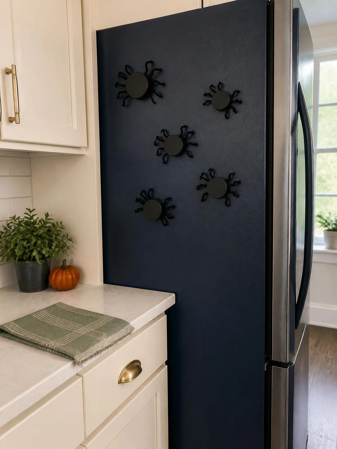 Black jar lid spider magnets decorate a navy refrigerator, showing a cheap DIY Halloween decoration for an indoor kitchen.
