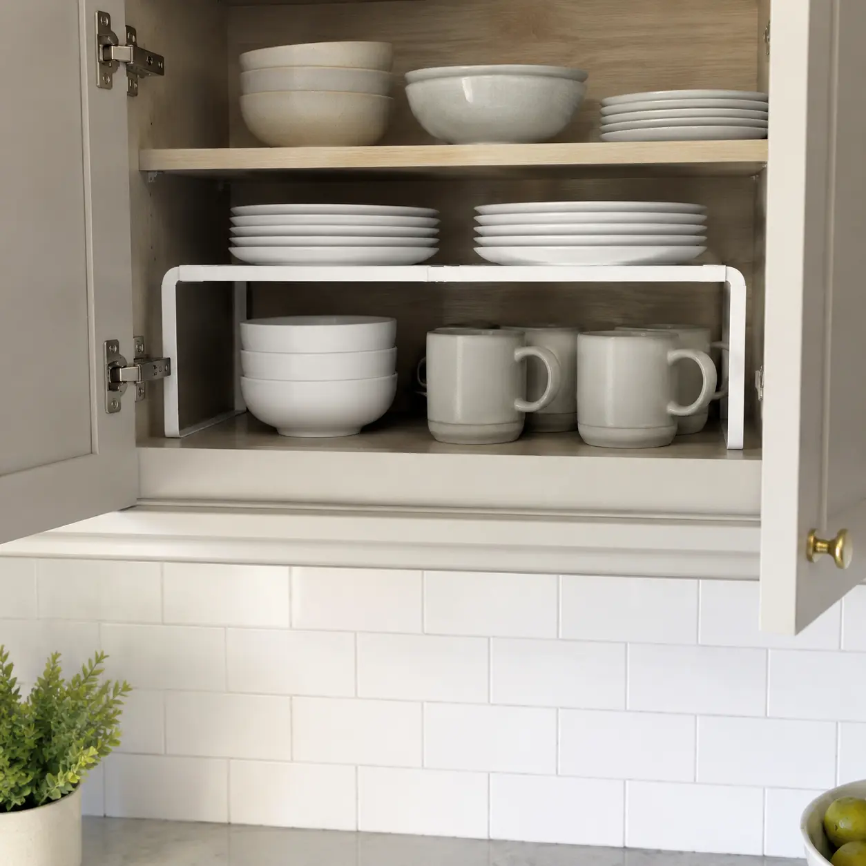 White metal shelf riser creating two levels for plates, bowls, and mugs
