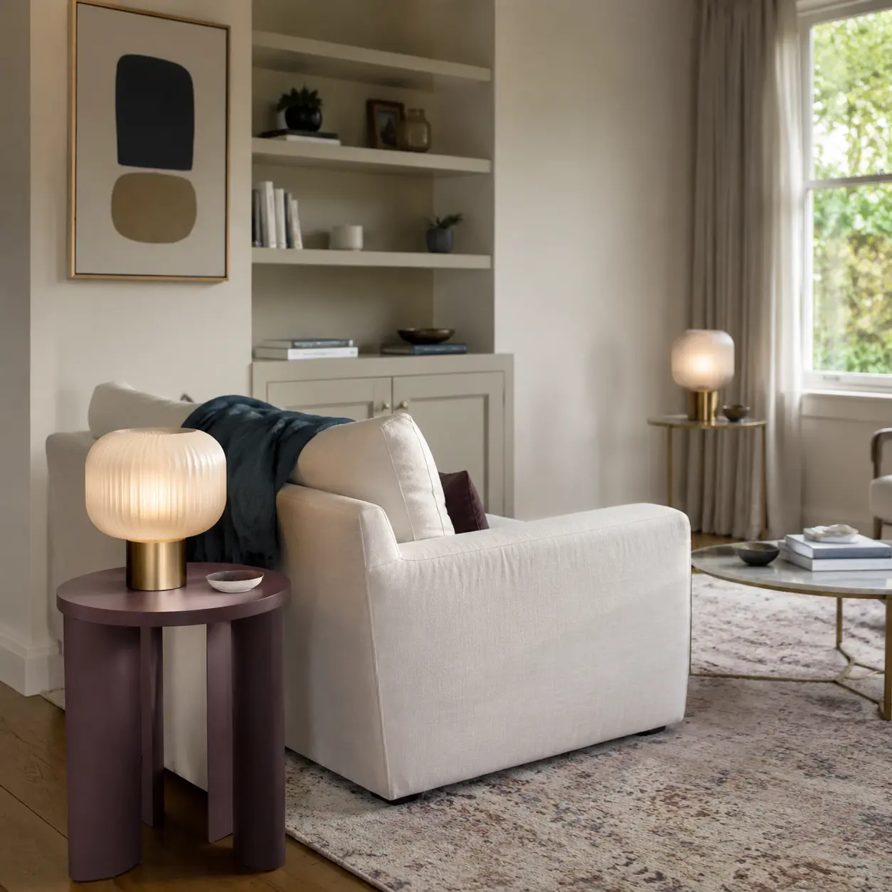 Mismatched plum and brass side tables connected by frosted glass lamps