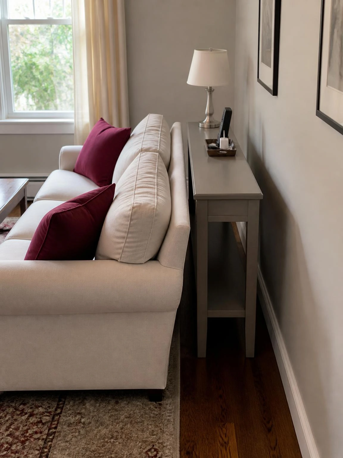 Slim warm-gray console behind an ivory sofa preserves a walking path in this small space living room, with lamp and charging tray.