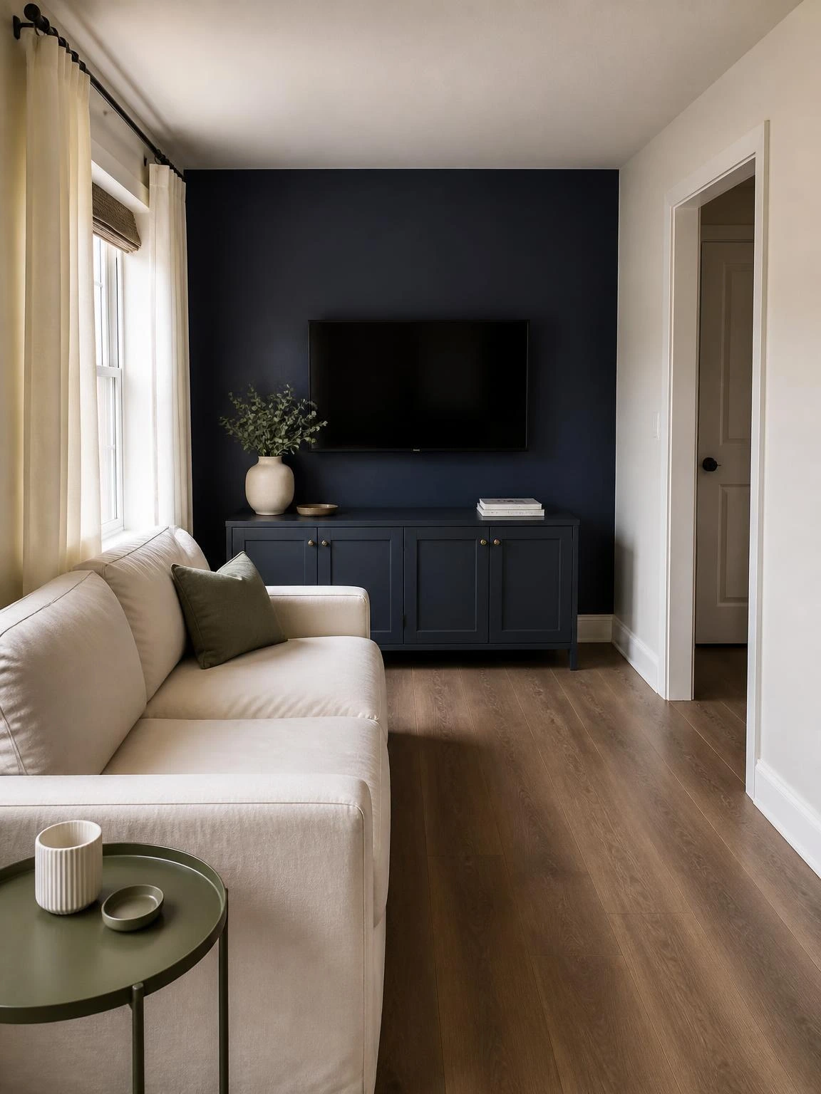 Narrow living room with an ivory sofa aligned to a navy focal wall, wall-mounted TV, low cabinet, and clear walking path