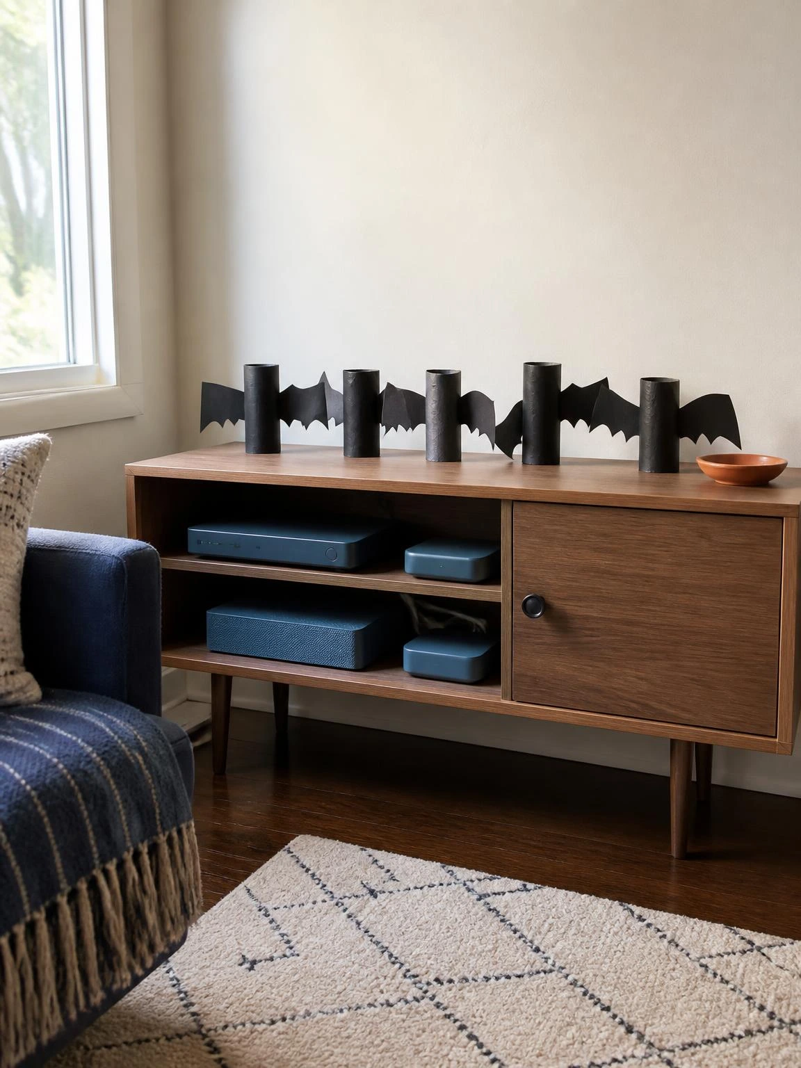 Black toilet paper roll bats perch on a compact media console, showing an easy cheap DIY Halloween decorations indoor project.
