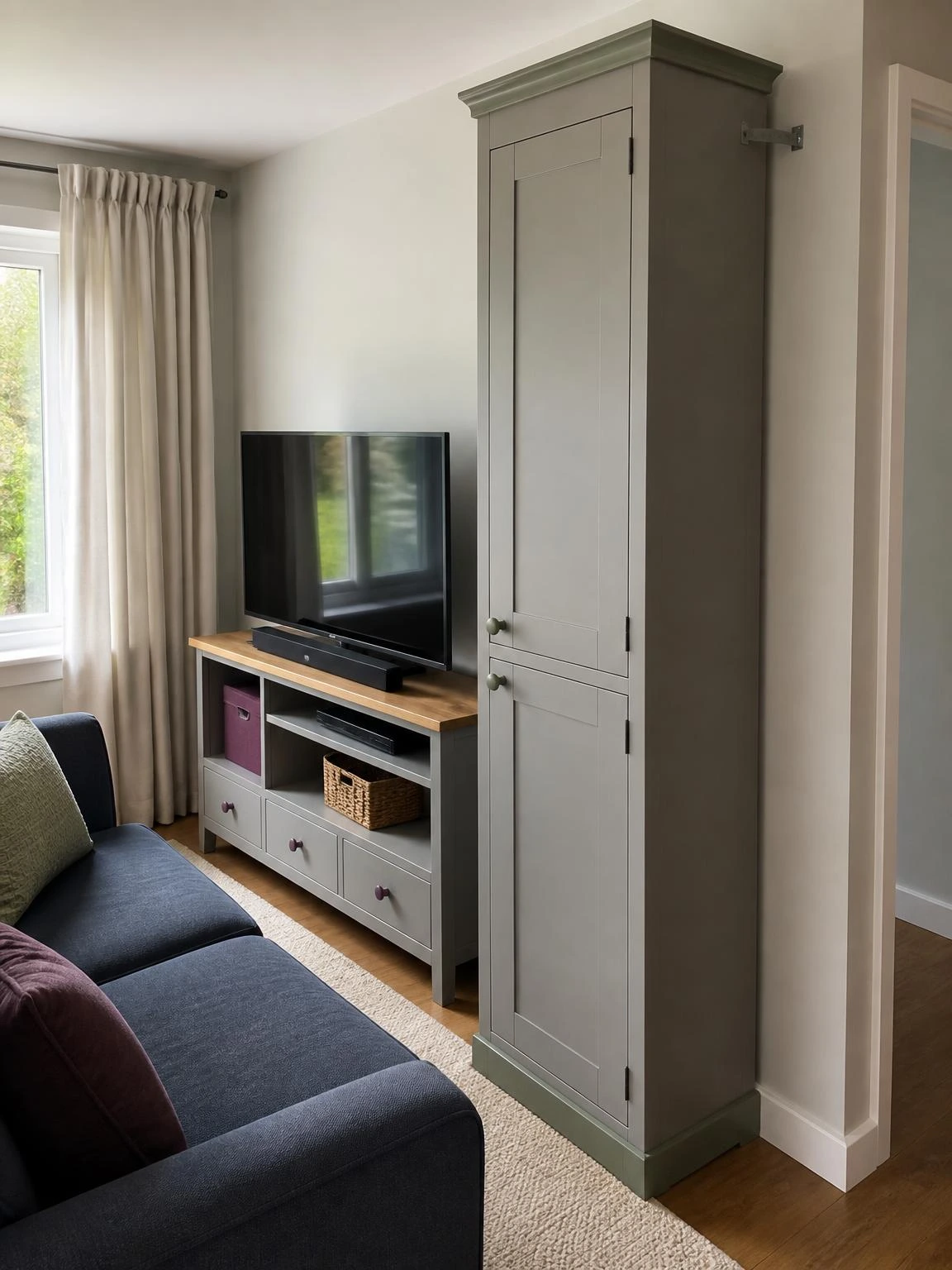 Tall narrow vertical cabinet beside a media unit uses wall height to organize storage in a compact living room